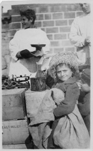 A photograph of a refugee boy with a hat receiving food.
