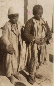 Two refugee boys dressed in scavenged clothing. The boy on the left is barefoot; the boy on the right wears shoes that are either improvised or severely damaged.
