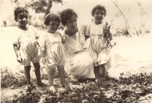 Nellie Mann with three children from the orphanage in Seydon Syria.  Mann,  kneeling embracing her three children who look happy and healthy. The four of them are in the woods.