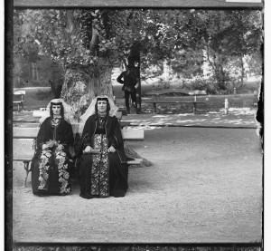 Two Armenian women wearing their folklore outfit, seating under a big tree.