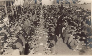 1400 orphan boys at a camp eating in tin plates. One relief workers and supervisors are supervising them.