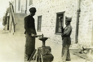 A man and boy practice smithing outdoors.