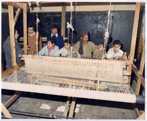 A man teaches a group of young boys to weave on a large loom in Egypt.