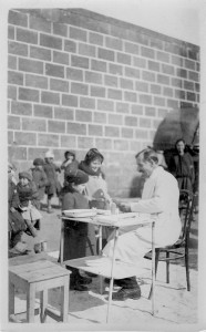 Dr. Russell Uhls ministers to patients in winter clothing in the orphanage courtard. Many of the first Near East Relief volunteers were physicians and nurses. Dr. Uhls was an ophthalmologist who specialized in the treatment and prevention of trachoma.