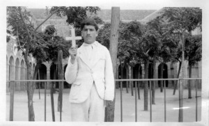 Young man in a suit holding a cross in a courtyard