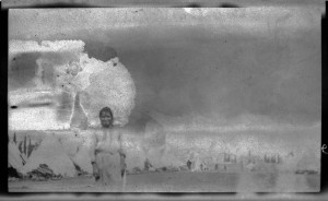 Damaged photograph of a refugee woman standing in front of a city of tents