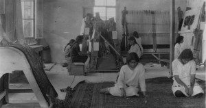 Young Armenian women weaving rugs in a small workplace with windows on the sides.