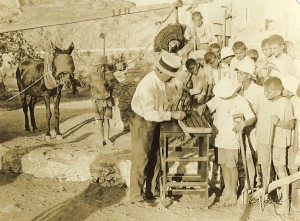 Relief worker and agricultural specialist Fred Midgley (in white hat) teaches farming skills to a group of Near East Relief orphans at the agricultural school at Syra. The children living at the Syra Orphanage were survivors of the genocides against the Ottoman Armenians and the Anatolian Greeks.
