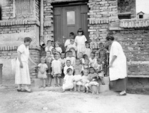 Very young orphan children with two relief workers in front of a dormitory at Kazachi Post orphanage, Alexandropol (now Gyumri), Armenia. The building is marked 