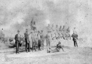 A group of men standing and sitting on a low wall. The men appear to be wearing uniforms. Date and location unknown.