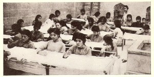 Near East Relief orphans working at the Aleppo, Syria needlework shop. The girls learned needlework, sewing, and embroidery as part of their vocational training. The products were sold in local shops to help benefit the orphanage. This photograph was featured in a 1924 New Near East article on orphan industries in Aleppo.