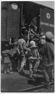 Children raising their hands to soldiers in uniform on a railway car. Children often begged at railway stops. The small child at left has bare feet and extremely ragged clothes. The writing and seal show that this was a Transcaucasian Railway car. H.C. Jaquith's notes identify this as either Batoum or Tiflis, 1920. Both cities were stops on the railway.