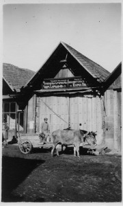 Man with a cow cart in front of a small building. The building sign, which is in both Armenian and Russian, announces that this is a library or reading room.