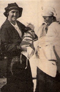Near East Relief worker Inez Webster presents a baby layette made by orphanage girls to a refugee mother. This photo appeared in the March 1927 issue of the New Near East magazine.