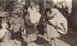 Smiling girls carrying bed rolls outside of an orphanage. This unlabeled photograph is probably from one of the girls' orphanages in Syria that Nellie Miller often visited, such as Seaside (Sidon) or Juniyeh.