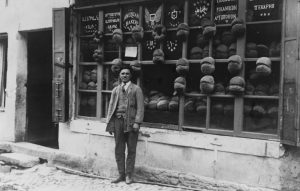 Baker stands in front of bakery with signs in five different languages.