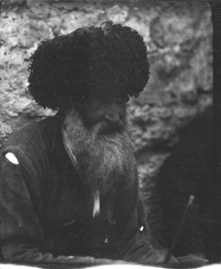 Bearded man with a ripped jacket and a large black hat. The wool hat is typical of the Caucasus region. 