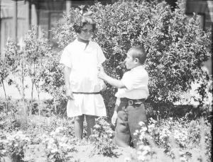 A boy presents a flower to a girl in the gardens at Alexandropol. Both wear orphanage uniforms. 